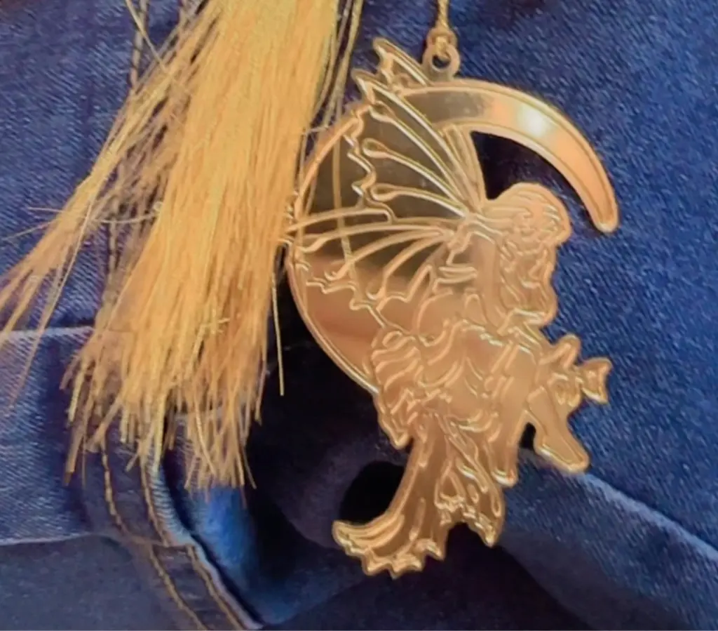 Metal bookmark that has a fairy sitting on the moon.
