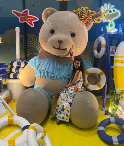 Heena from HeenaInTheWonderland is sitting in the lap of a giant teddy bear.