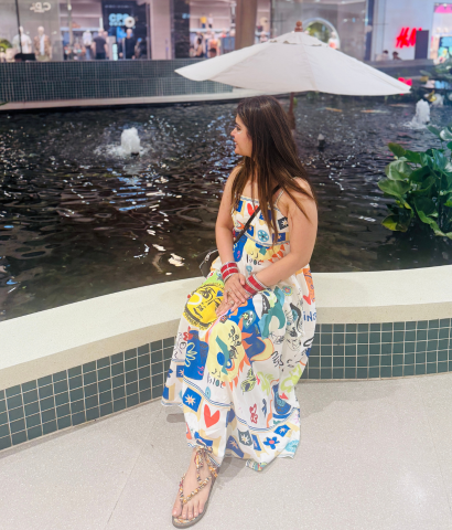 Heena from HeenaInTheWonderland is sitting in a colourful dress, smiling at the grandness of the Central Phuket Mall. 